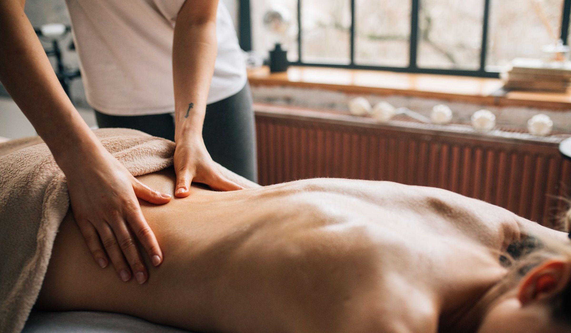 A massage therapist working on a client's back in warm daylight